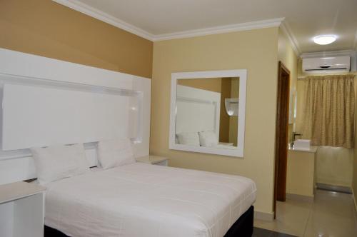 Un dormitorio con una cama blanca y un espejo. en PALACE LODGE PINETOWN, en Pinetown