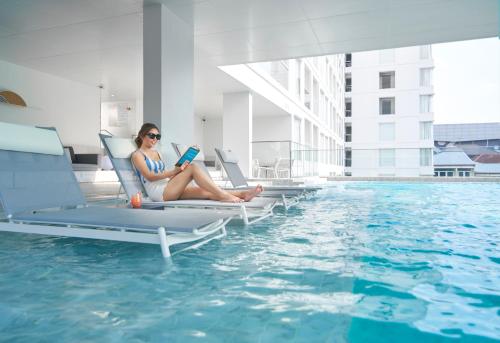 a woman sitting on lounge chairs reading a book next to a swimming pool at Shama Yen-Akat Bangkok in Bangkok
