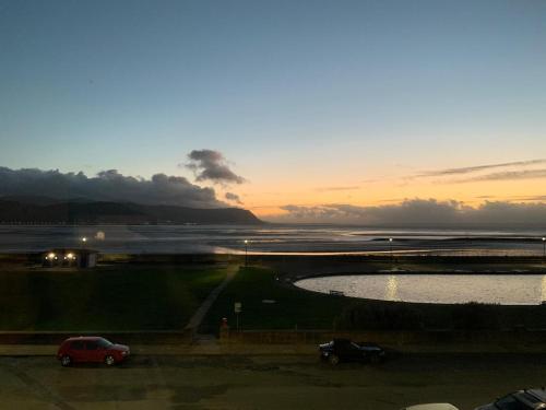 a sunset with two cars parked next to a body of water at Plas Gorwelion guest house - Adult only in Llandudno