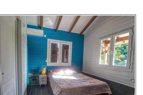 Cette chambre bleue comprend un lit et une fenêtre. dans l'établissement Magnifique maison en bois avec piscine, à Sainte-Anne