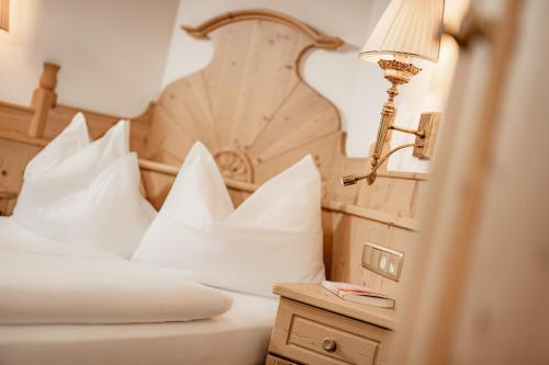 a bedroom with a bed with white pillows and a lamp at Romantik & Family Hotel Gardenia***S in Selva di Val Gardena