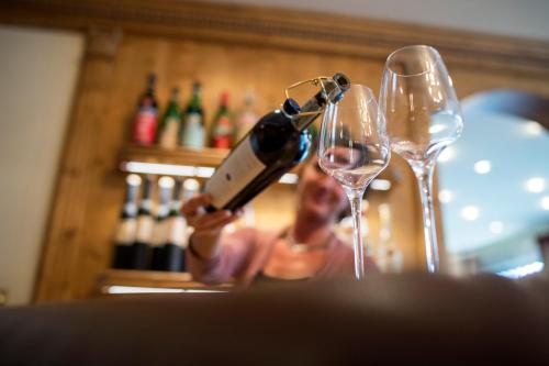 a woman is pouring wine into two wine glasses at Romantik & Family Hotel Gardenia***S in Selva di Val Gardena