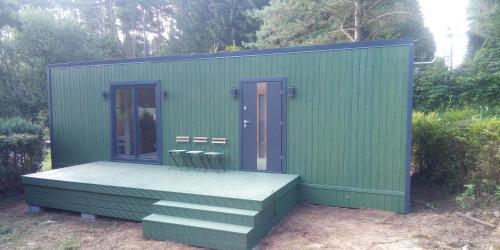 a green building with two doors and a deck at Haus "Blücher" TinyHouse Mobilheim in Stuer