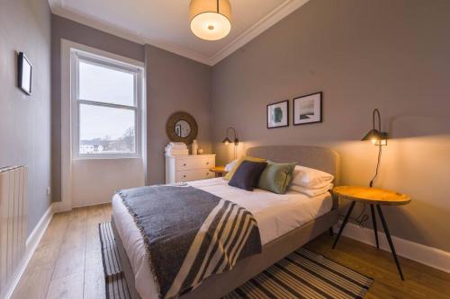 a bedroom with a bed with a table and a window at The Trossachs Apartment in Stirling