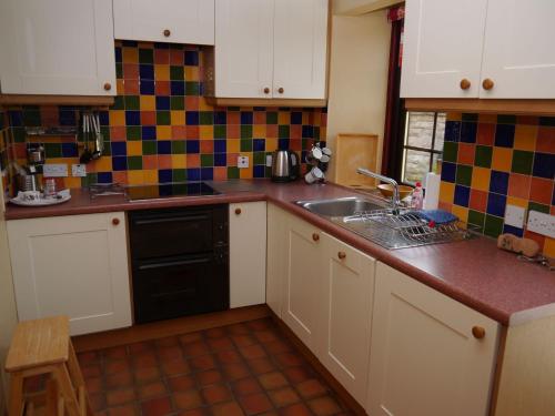 uma cozinha com armários brancos e um lavatório em Belmont Cottage em Dumfries