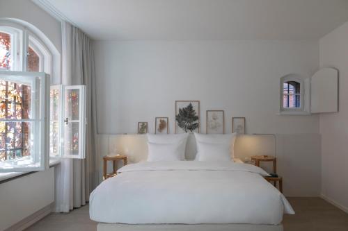 a white bedroom with a white bed and two windows at Wilmina Hotel in Berlin