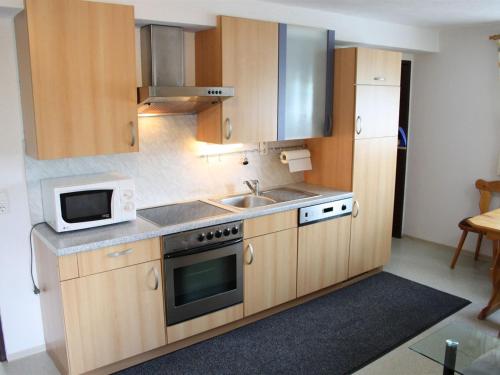 eine Küche mit Holzschränken, einer Spüle und einer Mikrowelle in der Unterkunft Lovely Chalet in Maria Alm with Terrace in Maria Alm am Steinernen Meer