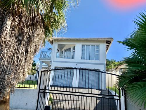 a white house with a gate and palm trees at Awesome Sea views! House near Zimbali in Densainagar