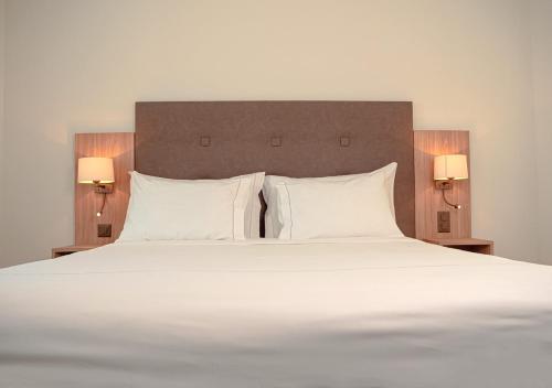 a large bed with white pillows and two lamps at Auberge Le Relais in Chavannes-de-Bogis