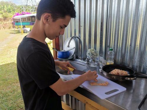a young man cutting up carrots on a cutting board at Dreamcatcher House Bus Experience 2 in Sarchí