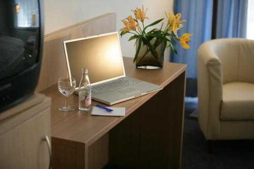 einen Laptop auf einem Tisch mit Brille und eine Vase Blumen in der Unterkunft Hotel Senator München in München