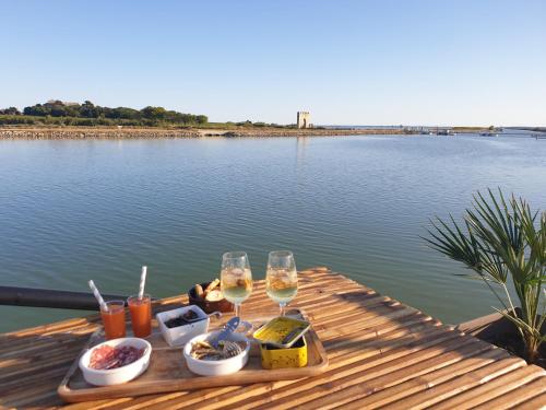 a table with two glasses of wine and food on a lake at Peniche Alphonsia Maria in Villeneuve-lès-Maguelonne
