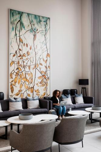 a woman sitting on a couch in a living room with a laptop at The Capital Trilogy Menlyn Maine in Pretoria