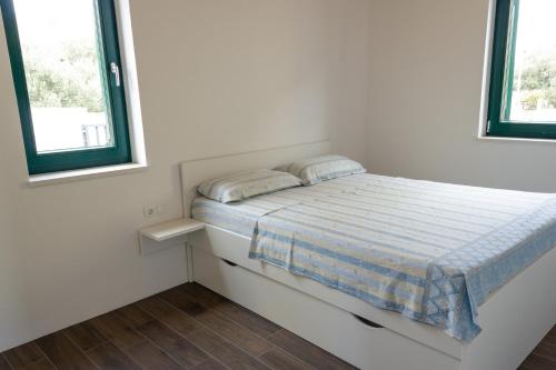 a bed in a white room with two windows at Apartments Dujic in Tribunj