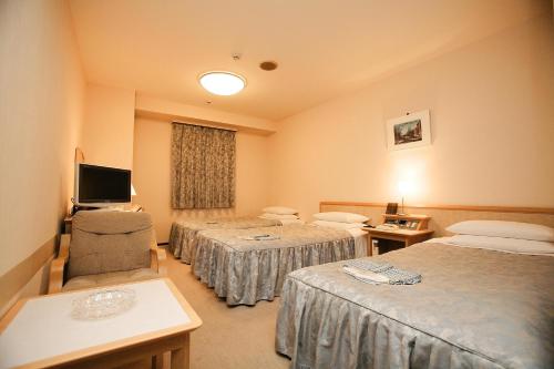 a hotel room with three beds and a television at Narita U-City Hotel in Narita