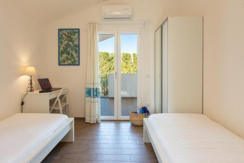 1 dormitorio con 2 camas, escritorio y ventana en Sardinia Hostay Holiday House With Garden Sant'Isidoro, en Sant' Isidoro