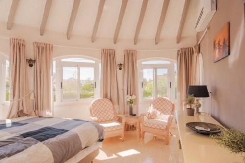 a bedroom with a bed and two chairs and windows at Casa Kollies in Calpe