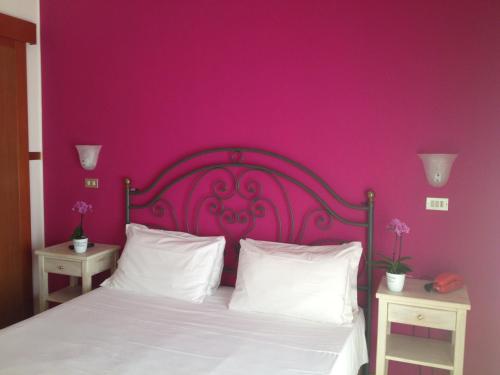 a bedroom with a pink wall and a bed with white pillows at Hotel Benacus in Lazise