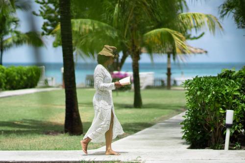 a woman walking down a sidewalk near the beach at Antigua Village Beach Resort in Saint Johnʼs