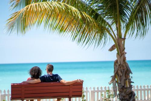 a man and woman sitting on a bench near the beach at Antigua Village Beach Resort in Saint Johnʼs