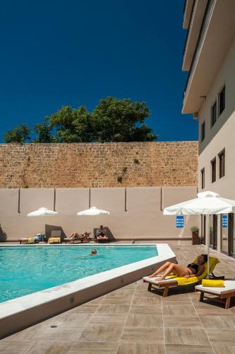a pool with two people sitting on lounge chairs next to a building at Kriti Hotel in Chania Town