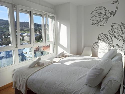2 weiße Betten in einem Zimmer mit Fenstern in der Unterkunft Apartamento PATXIKE con plaza de garaje in Bermeo