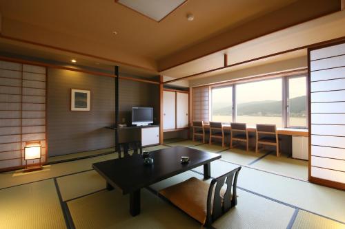 a room with a table and chairs and a television at Rako Hananoi Hotel in Suwa