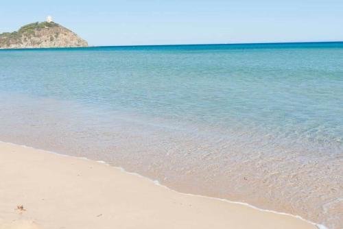 a beach with blue water and an island in the background at Appartamento in Villa Gelsomino in Domus de Maria