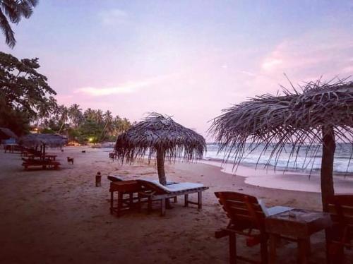 a beach with tables and chairs and a straw umbrella at Deshan Homestay & Restaurant in Tangalle