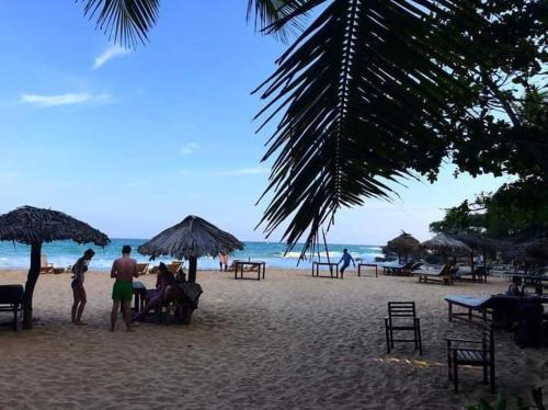 a group of people on a beach with chairs and umbrellas at Deshan Homestay & Restaurant in Tangalle