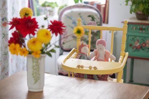 two dolls sitting in a chair on a table with a vase of flowers at Maison Léontine in Bernay