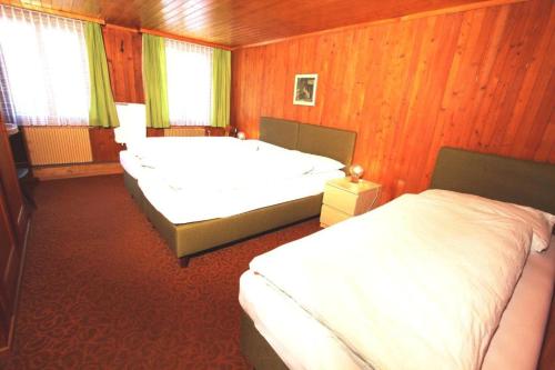 two beds in a bedroom with wood paneling at Hotel-Restaurant Alpina in Innertkirchen