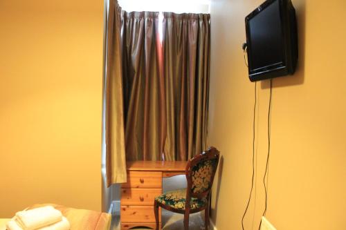 a room with a chair and a desk and a television at Skylark Guest House in Hounslow