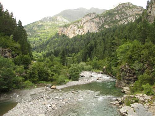 a river in the middle of a valley with mountains at La Casita de Ordesa in Frajén