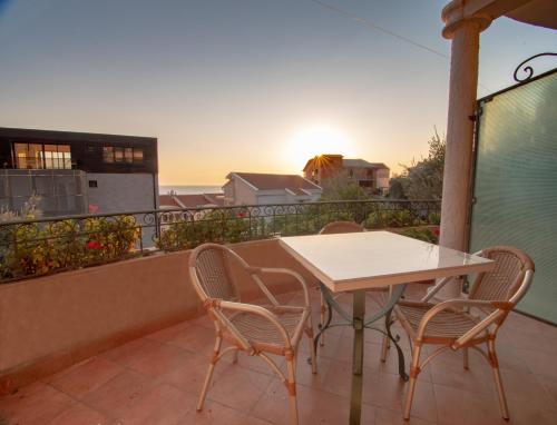 a table and chairs on a balcony with the sunset at Apartments and Rooms Levantin Inn in Sveti Stefan
