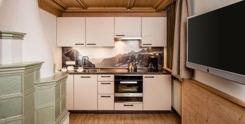 a kitchen with white cabinets and a tv at Apartments Villa Gardena - Gardenahotels in Selva di Val Gardena