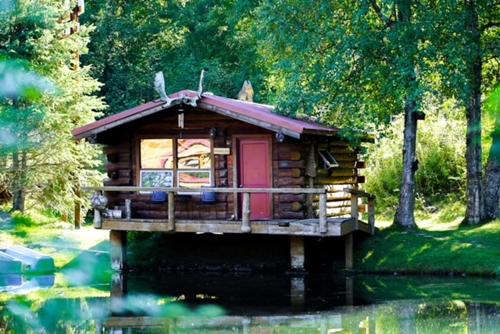 a log cabin with a red door on a pond at Hope Alaska's Bear Creek Lodge in Hope