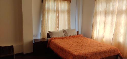 a bedroom with a bed with an orange comforter and curtains at Crossroad in Shillong