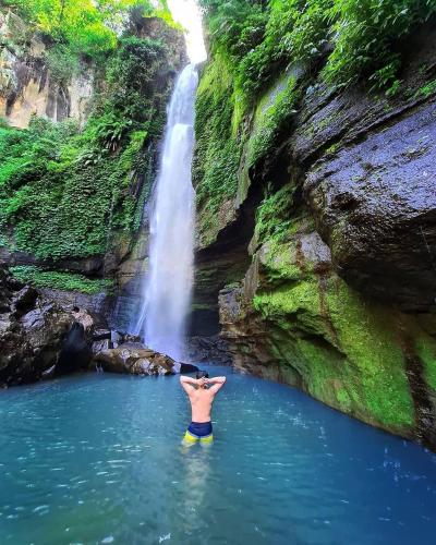 a man standing in a pool of water in front of a waterfall at Pagupon Camp Syariah in Batu