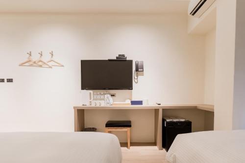 a bedroom with a desk with a tv on a wall at Traveller-Inn Day Moon Hotel in Taitung City