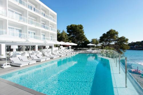 una piscina con sillas blancas y un edificio en Grupotel Ibiza Beach Resort - Adults Only, en Portinatx