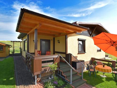 ein kleines Haus mit einer Terrasse und einem orangenen Regenschirm in der Unterkunft Holiday home near the Schwarza Valley in Grossbreitenbach