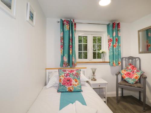 a bedroom with a bed and a chair and a window at Heligan Cottage in St Austell