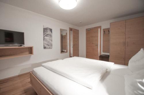 a bedroom with a white bed and a flat screen tv at Gästehaus Sonne in Bichlbach