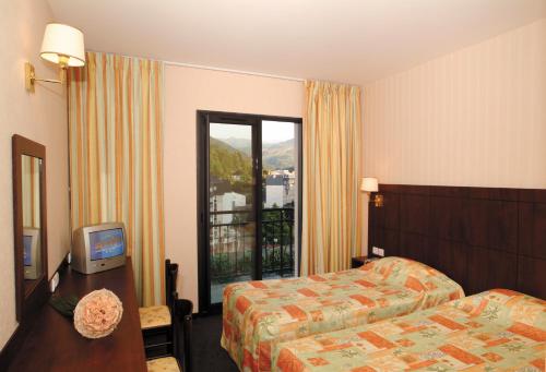 a hotel room with a bed and a tv and a window at Hôtel Gloria & Avenue in Lourdes