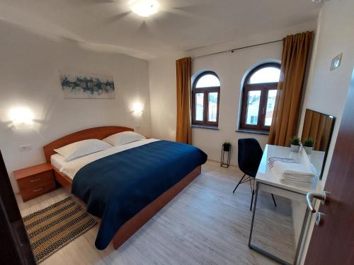 a bedroom with a bed and a desk and two windows at Apartments Amfora in Barbat na Rabu