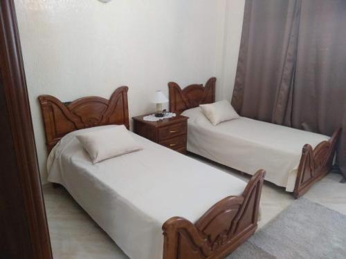 two twin beds in a room with a night stand at Appartement Bio Meknes Hamria in Meknès