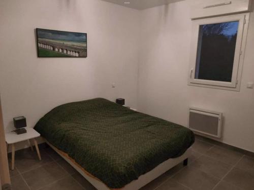 a bedroom with a bed with a green comforter and a window at Maison individuelle neuve plein pied avec terrasse et jardin clos 10minutes a pied de la plage in Quiberville