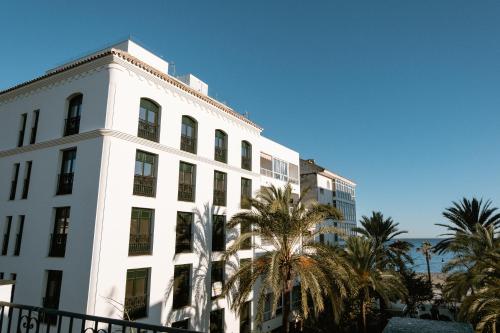 Hotel Estepona Plaza في إِستيبونا: مبنى أبيض مع أشجار النخيل أمام المحيط