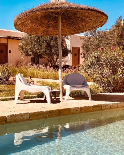 two chairs and an umbrella next to a swimming pool at Dar Alya Essaouira Maison et table d'hôtes in Ghazoua